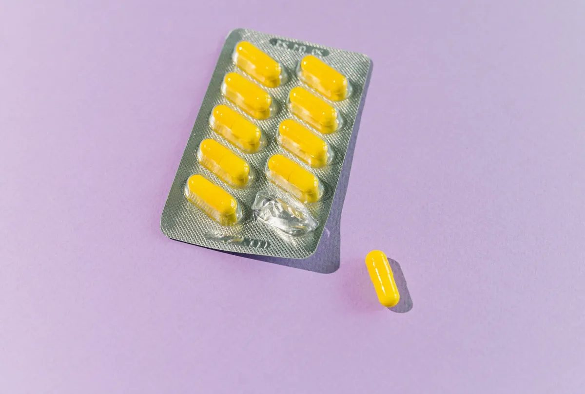 A blister pack of yellow capsules with one pill on a purple backdrop.