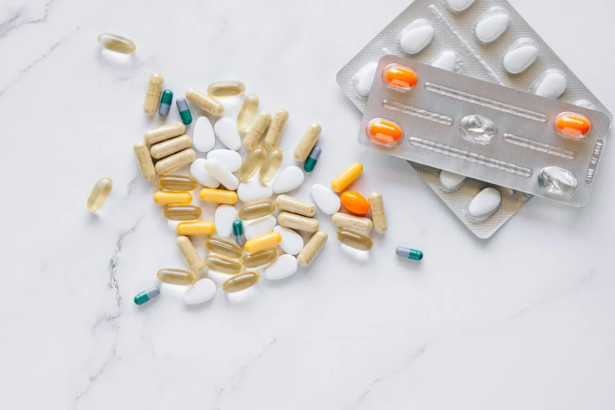 A variety of colored capsules and tablets arranged on a white marble surface, alongside blister packs.